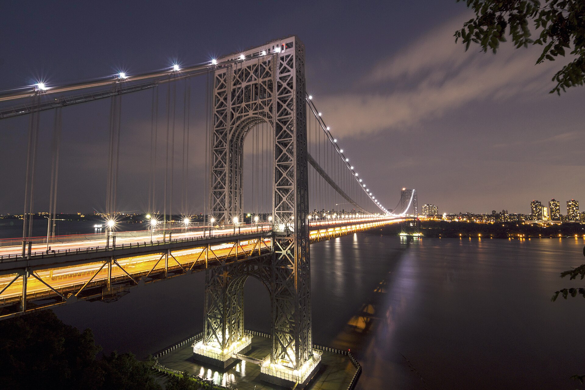 The George Washington Bridge illuminated at night with streaks of rush-hour traffic crossing the Hudson