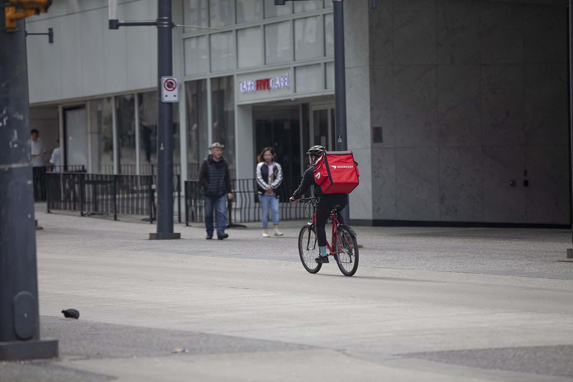 DoorDash buys Instacart deal — a DoorDash courier with a red delivery backpack rides a bicycle along Granville Street in downtown Vancouver, a file photograph from March 2020