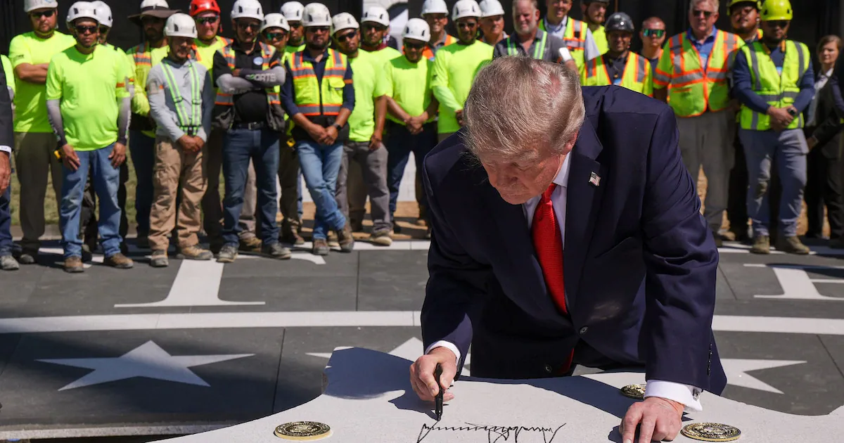 President Donald Trump signs the renovated White House helipad in front of construction workers