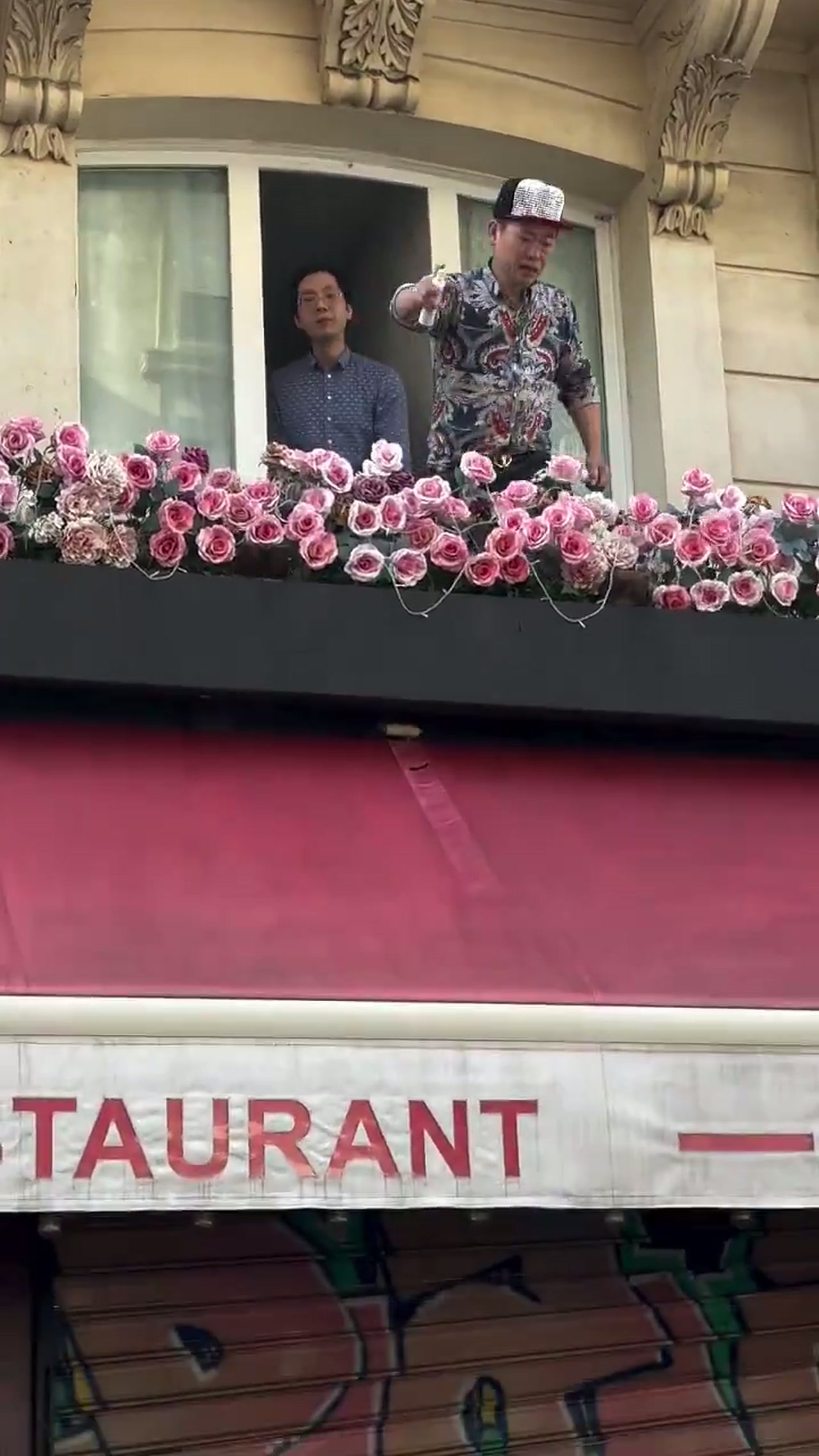 A man on the balcony above La Barrique restaurant in Paris spraying an aerosol down at a crowd during the France riots, in the viral Paris café perfume video