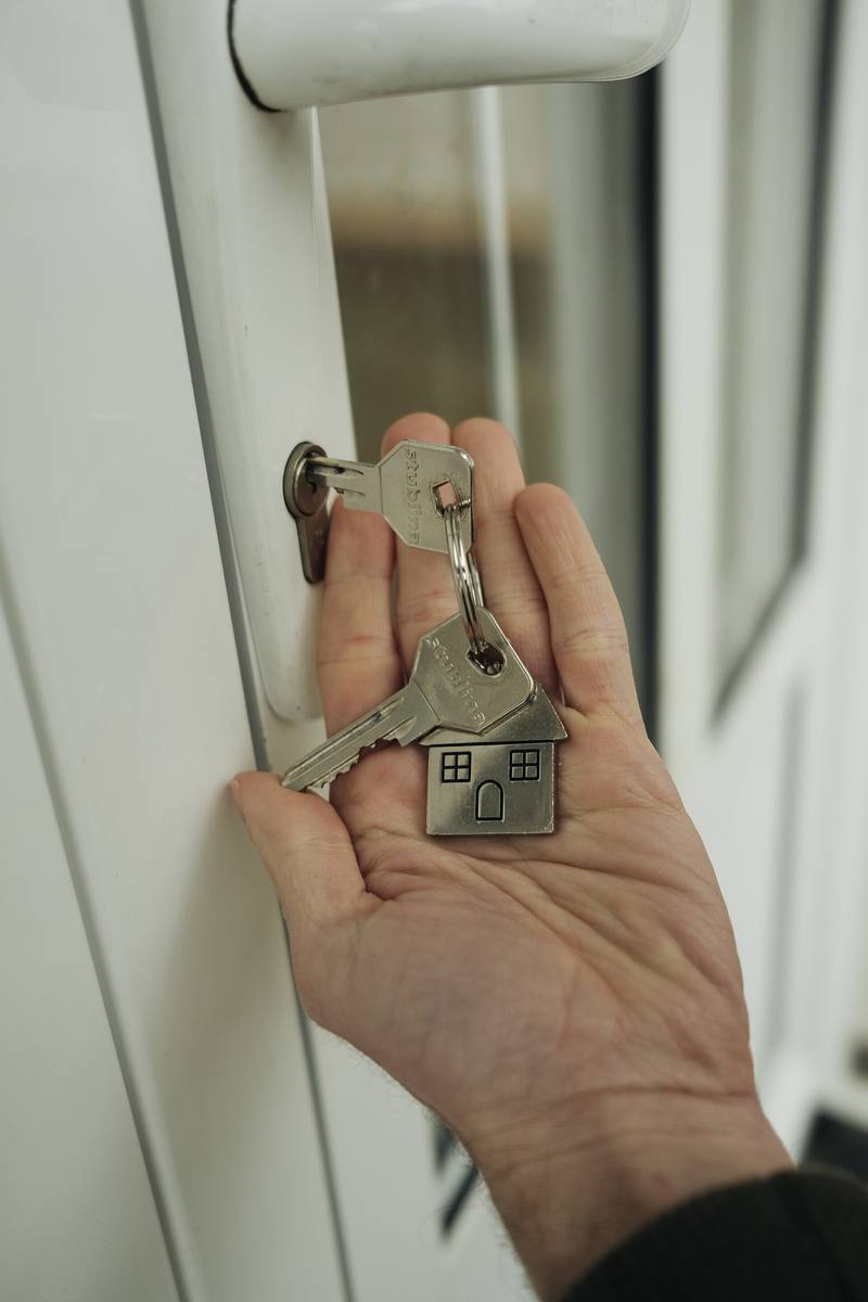 A hand holding house keys near a door lock, symbolizing a first-time home purchase
