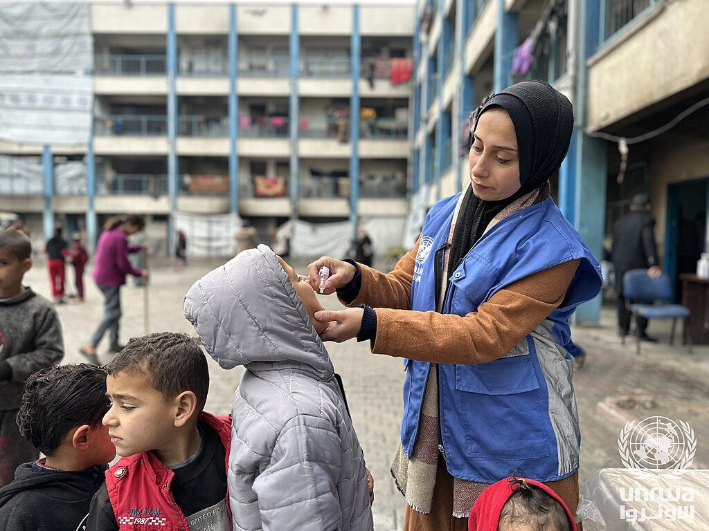 A health worker in a UNRWA vest gives oral polio vaccine drops to a young child at an UNRWA shelter in Beach camp, Gaza Strip — Gaza children health file photograph