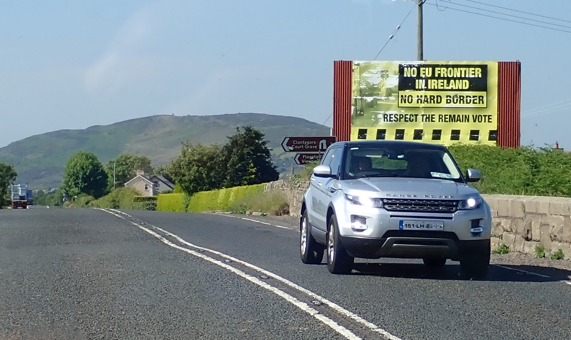 A car crosses the Ireland–Northern Ireland border at Killeen Bridge beside a 'No Hard Border' sign — the open border a unity referendum would remove