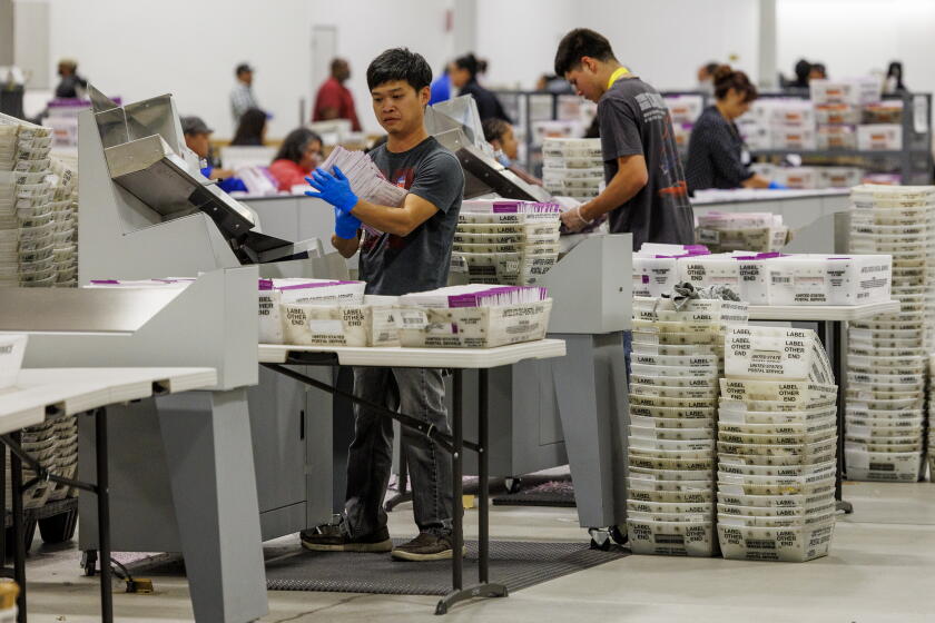Election workers process vote-by-mail ballots amid stacks of ballot trays at the Los Angeles County Ballot Processing Center in the City of Industry, California