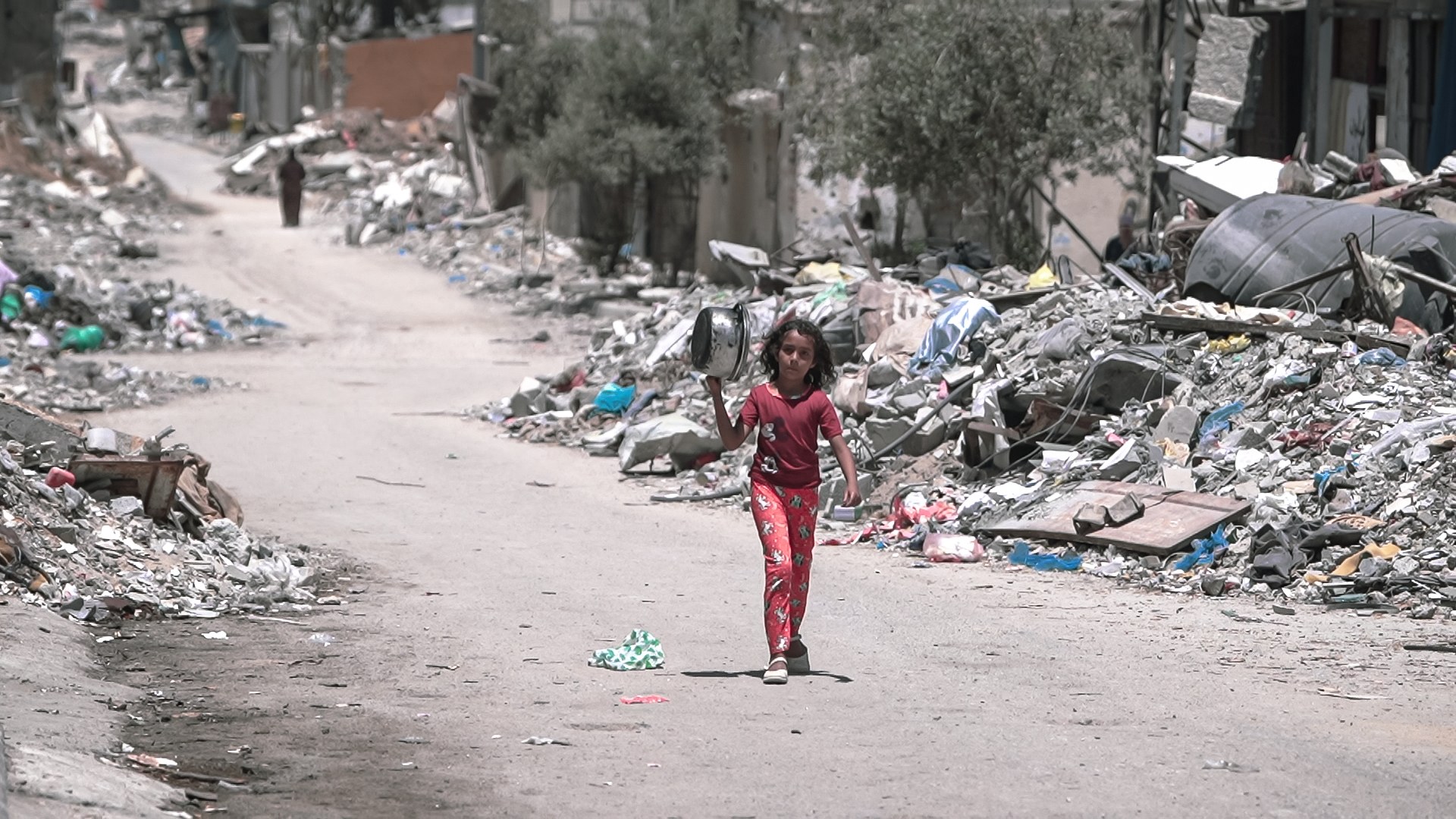 A young girl carries a cooking pot through a rubble-lined street in Gaza on her way to collect food — Gaza commercial goods halt file photograph