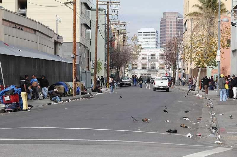 A Skid Row street in downtown Los Angeles with tents, pedestrians and downtown buildings