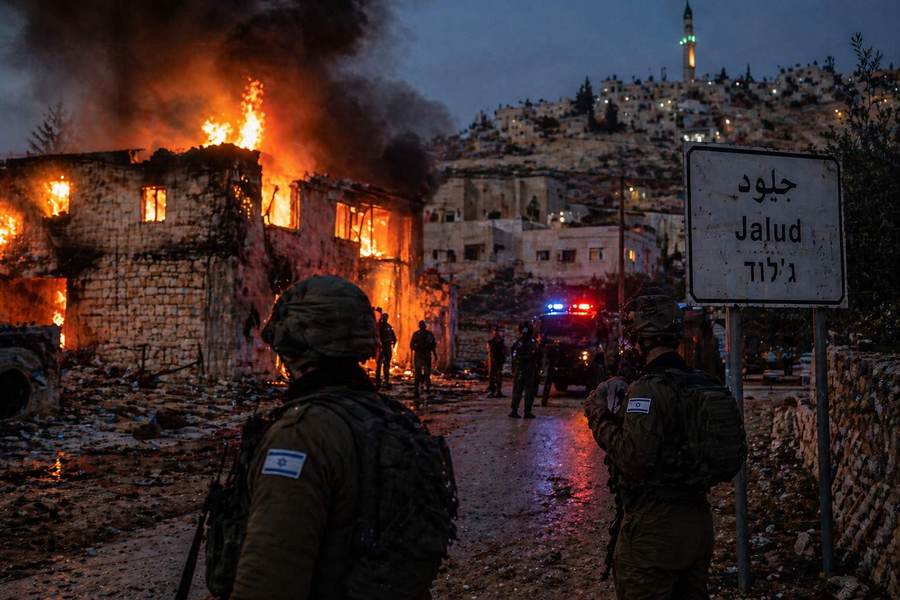 A building burns in Jalud during a settler arson attack earlier in 2026, with the Jalud road sign and Israeli forces visible