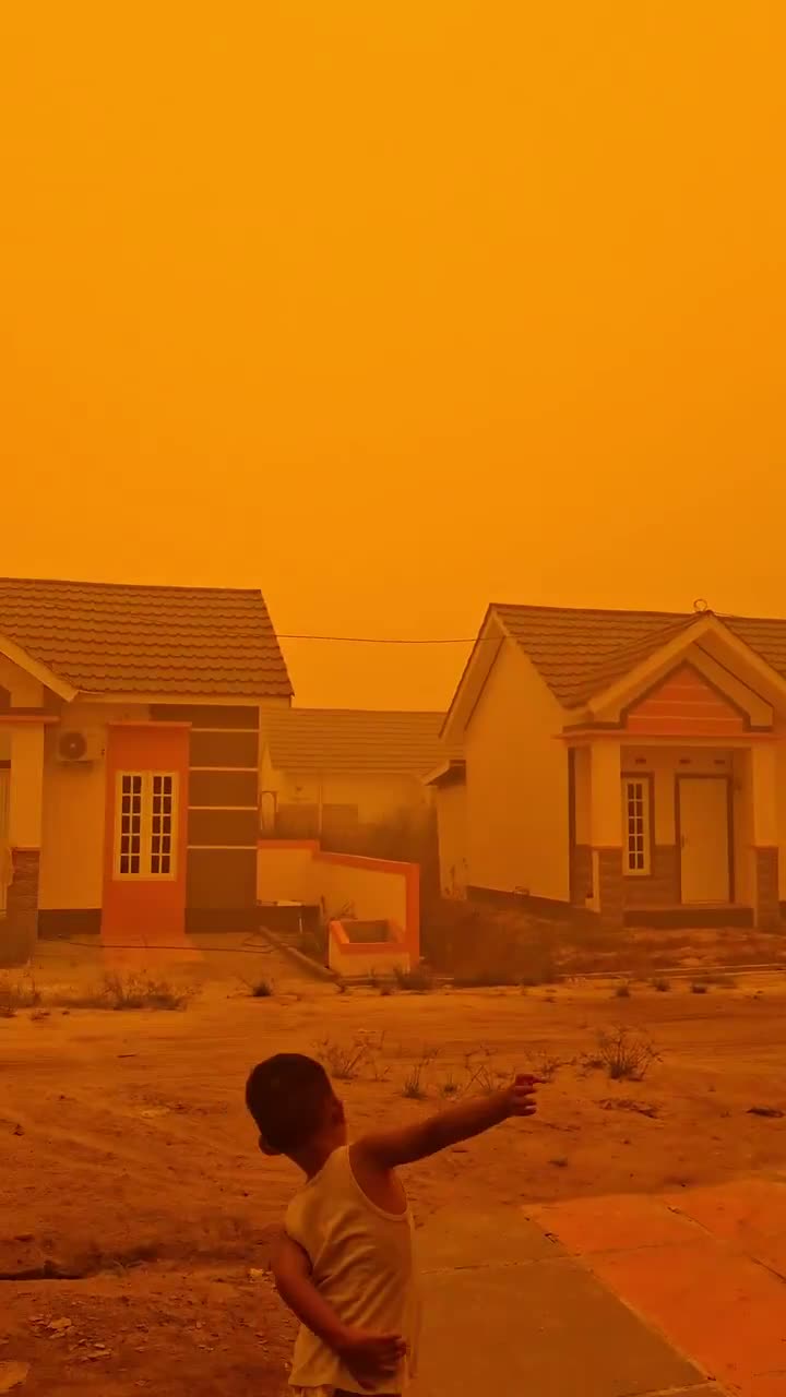 A child points at an orange sky over a housing estate in Palangka Raya, Central Kalimantan, during the Indonesia haze, October 2026